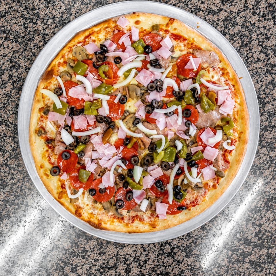 Whole pizza with pepperoni, ham, green peppers, onions, black olives, and mushrooms on a metal tray.