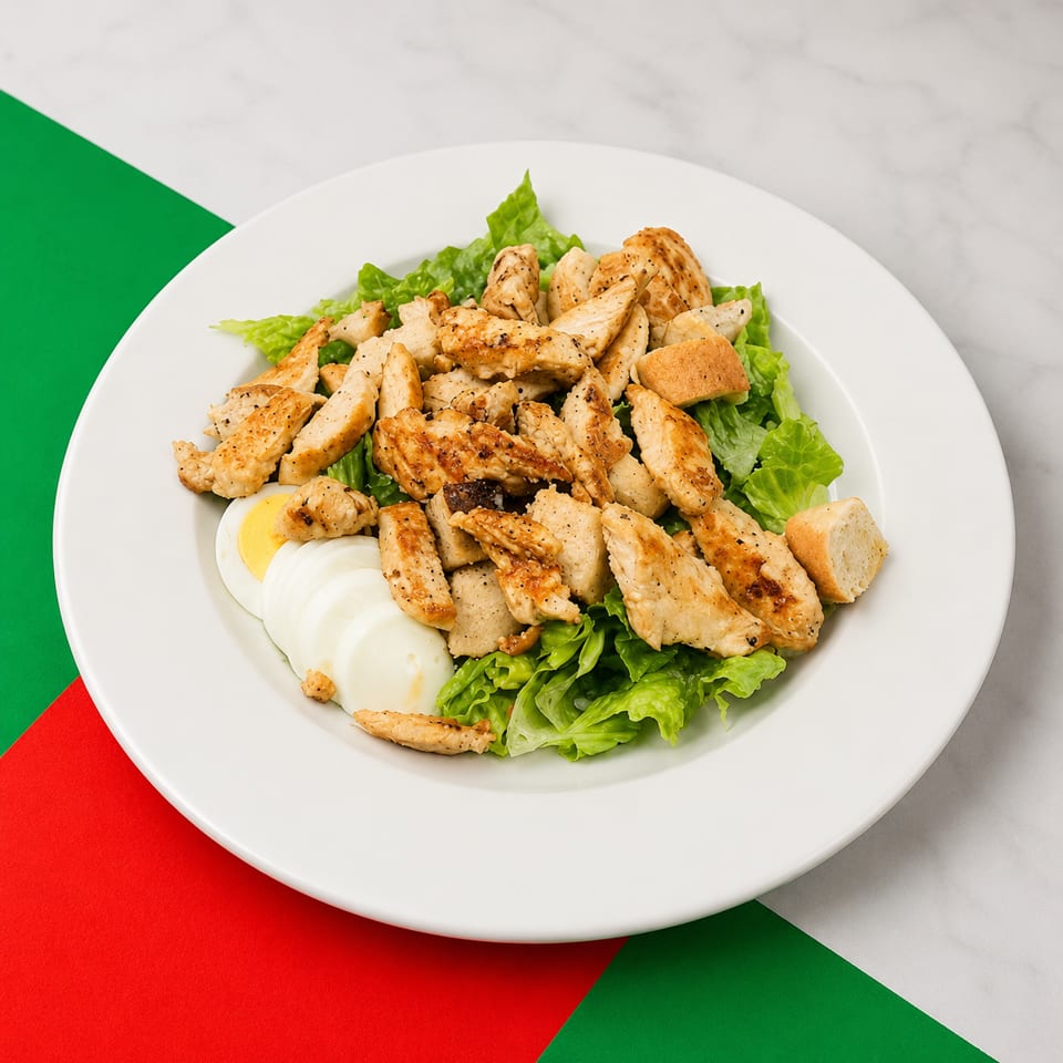 Grilled chicken salad with lettuce, sliced egg, and croutons on a white plate.